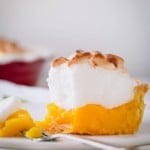 A slice of classic lemon meringue pie on a plate with a fork holding a bite.