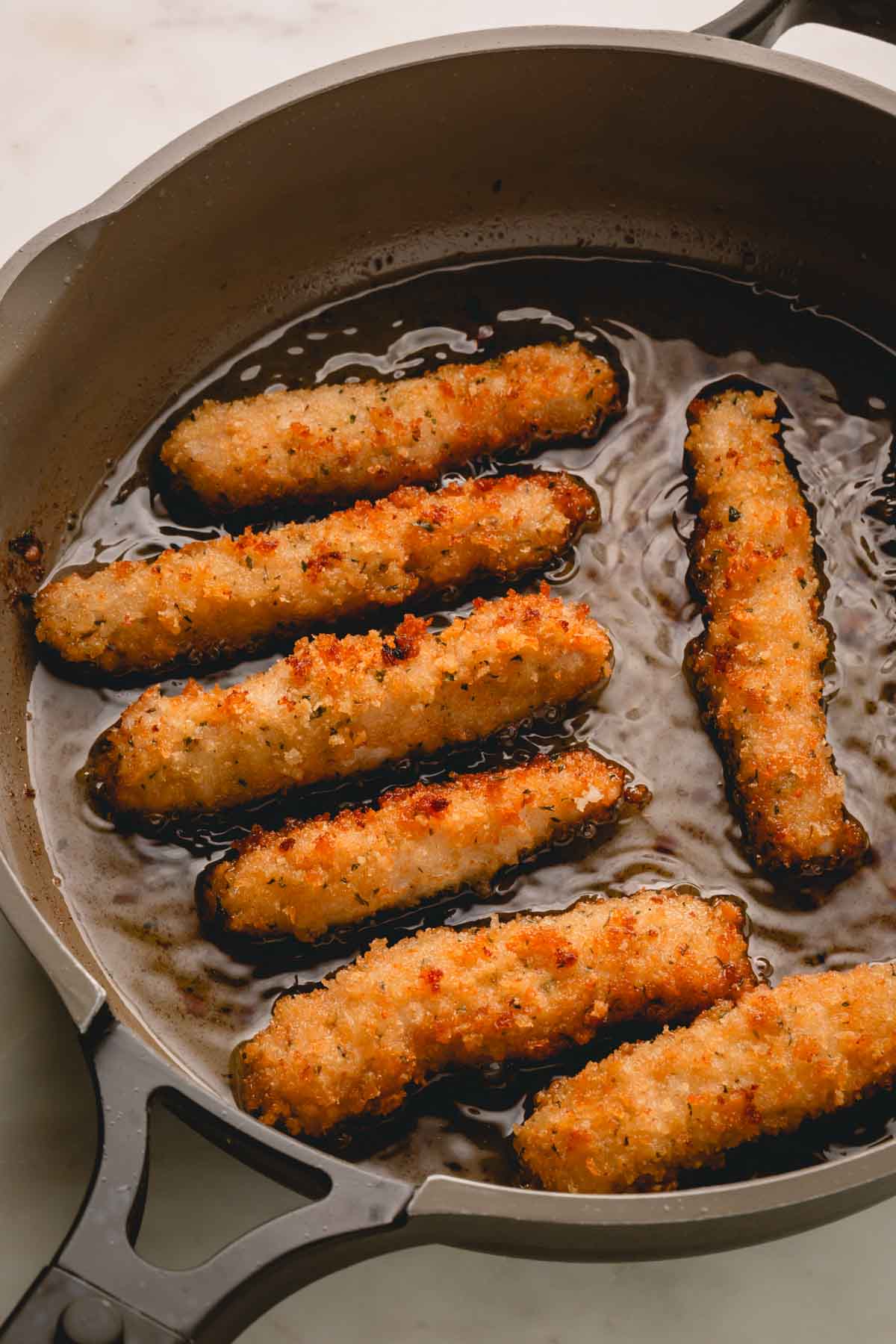 Pork strips cooking in oil in a skillet.