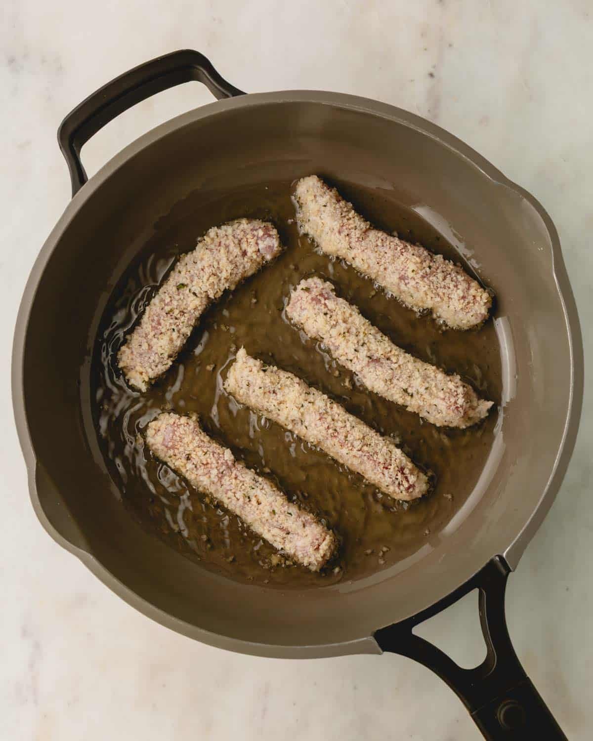 Breaded pork strips cooking in oil in a skillet.