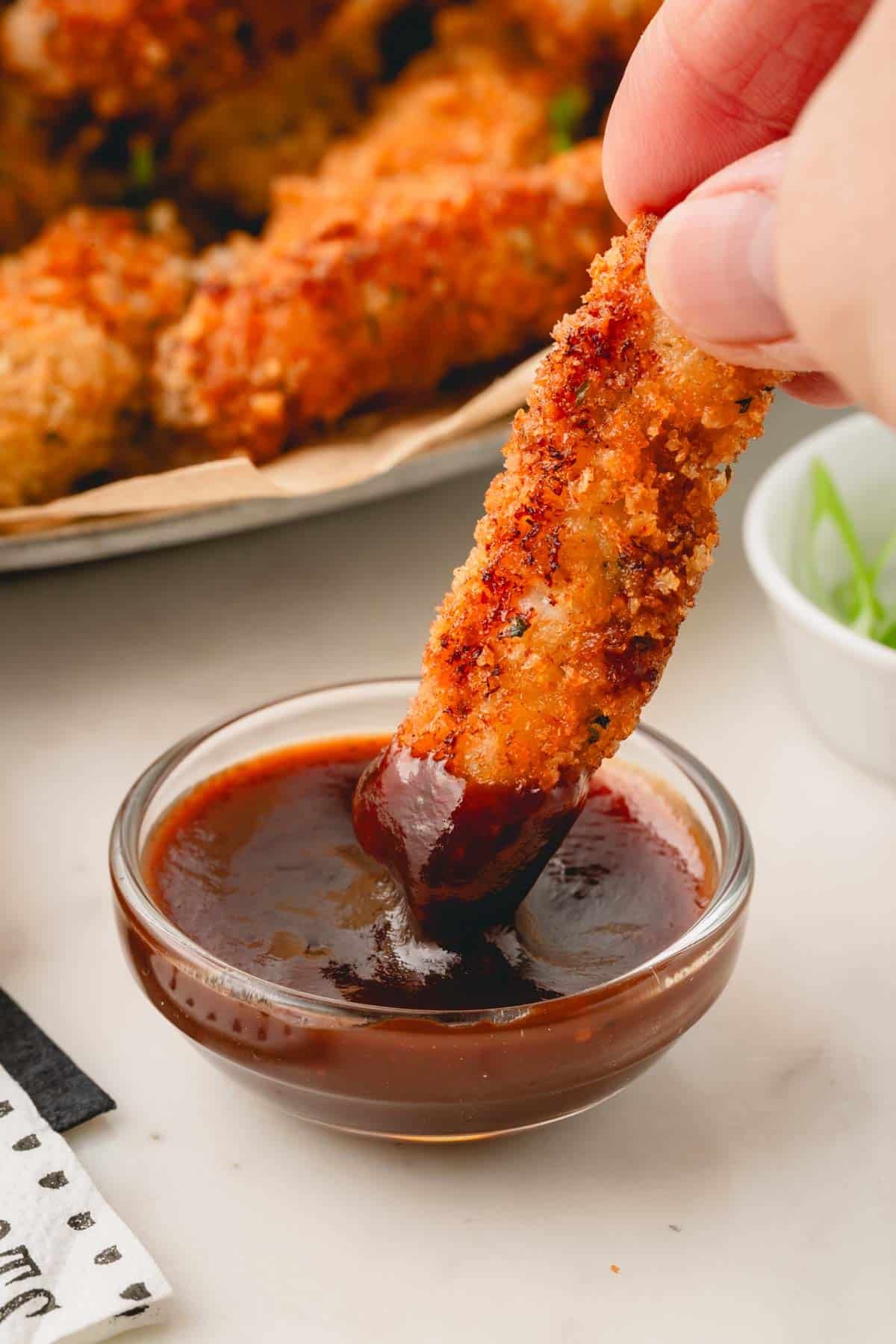 A pork strip being dipped in a bowl of BBQ sauce.