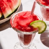 A glass of frozen watermelon daiquiri garnished with a slice of lime.