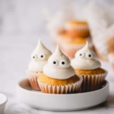 3 mini pumpkin muffins on a white plate topped with domed cream cheese frosting and candy eyes.