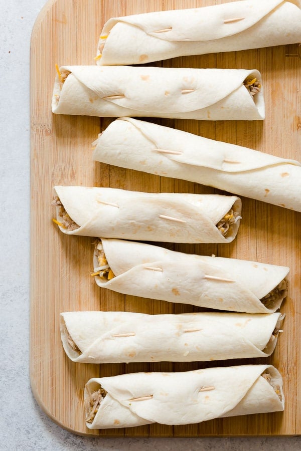 Uncooked pulled pork flautas secured with toothpicks.