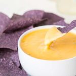 A chip being dipped into a bowl of spicy cheddar cheese dip.