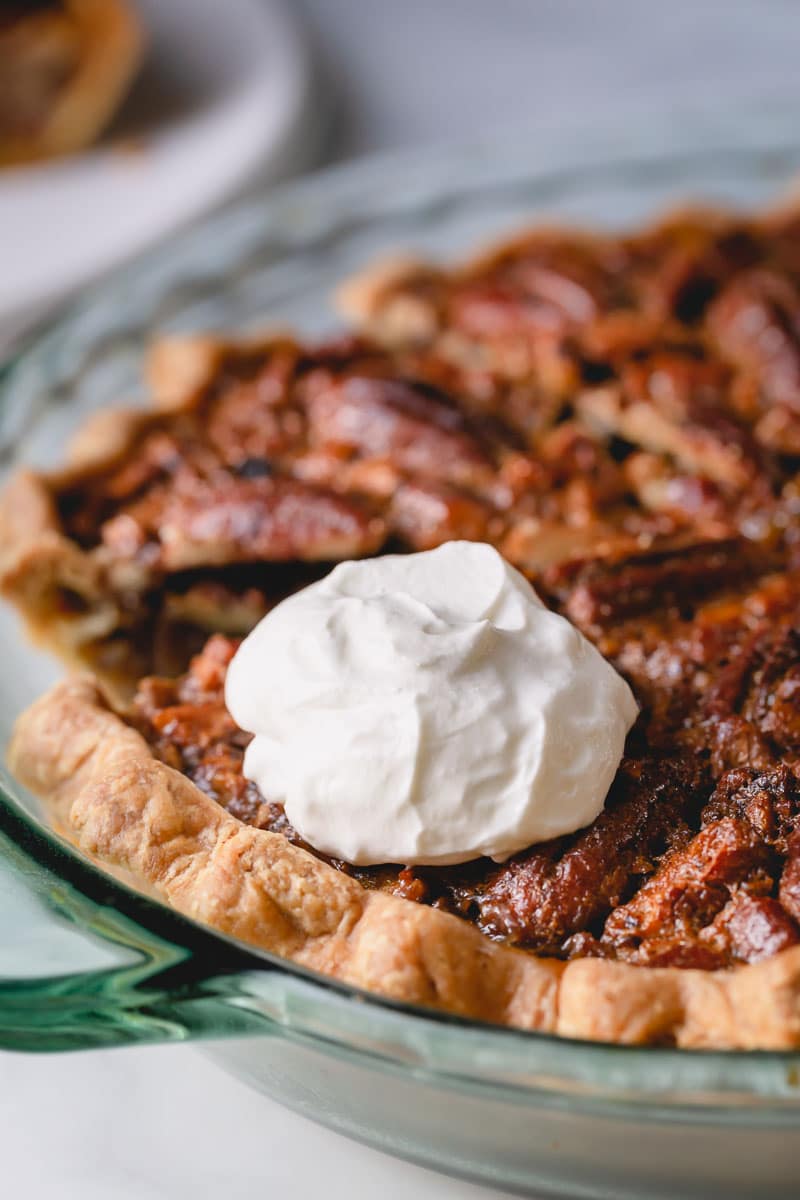 Pecan pie in a pie dish with a dollop of whipped cream on top.