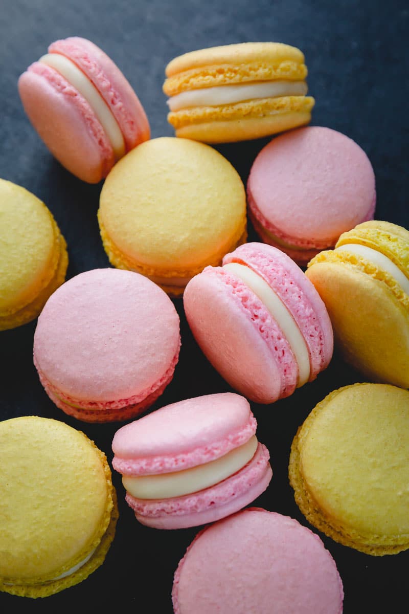 Yellow and pink macarons filled with white chocolate ganache arranged on a dark surface