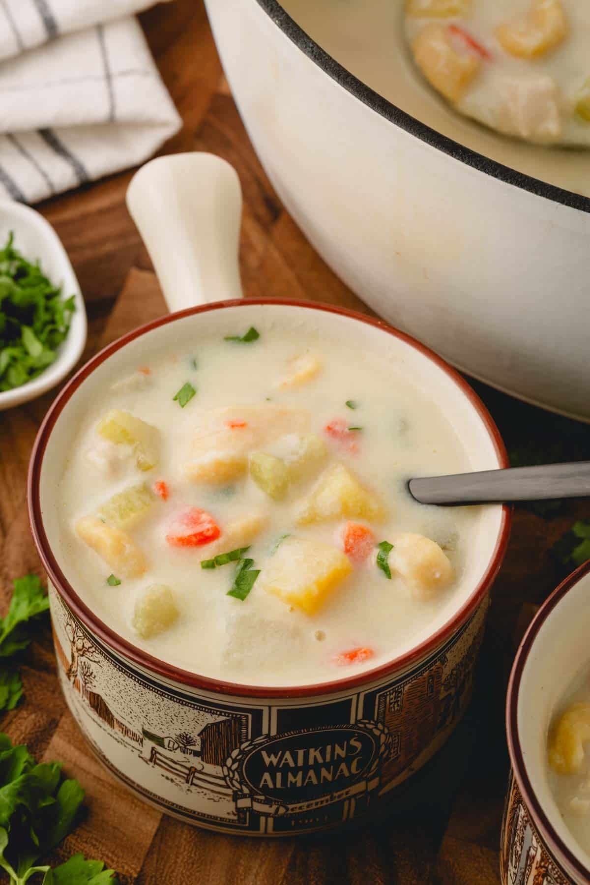 A bowl of knoephla soup next to a pot of soup.