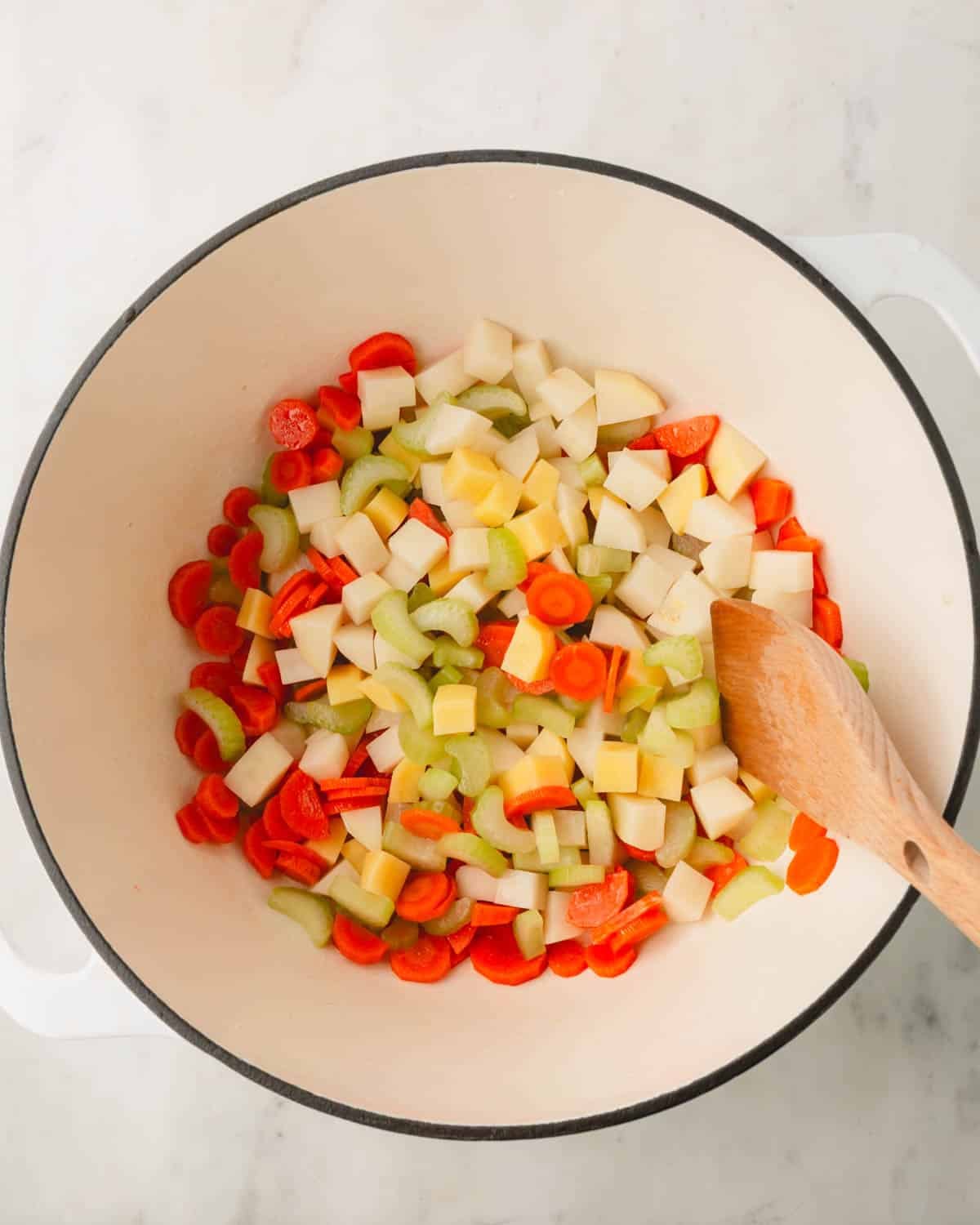 Chopped carrots, celery, and potatoes in a Dutch oven with a wooden spoon.