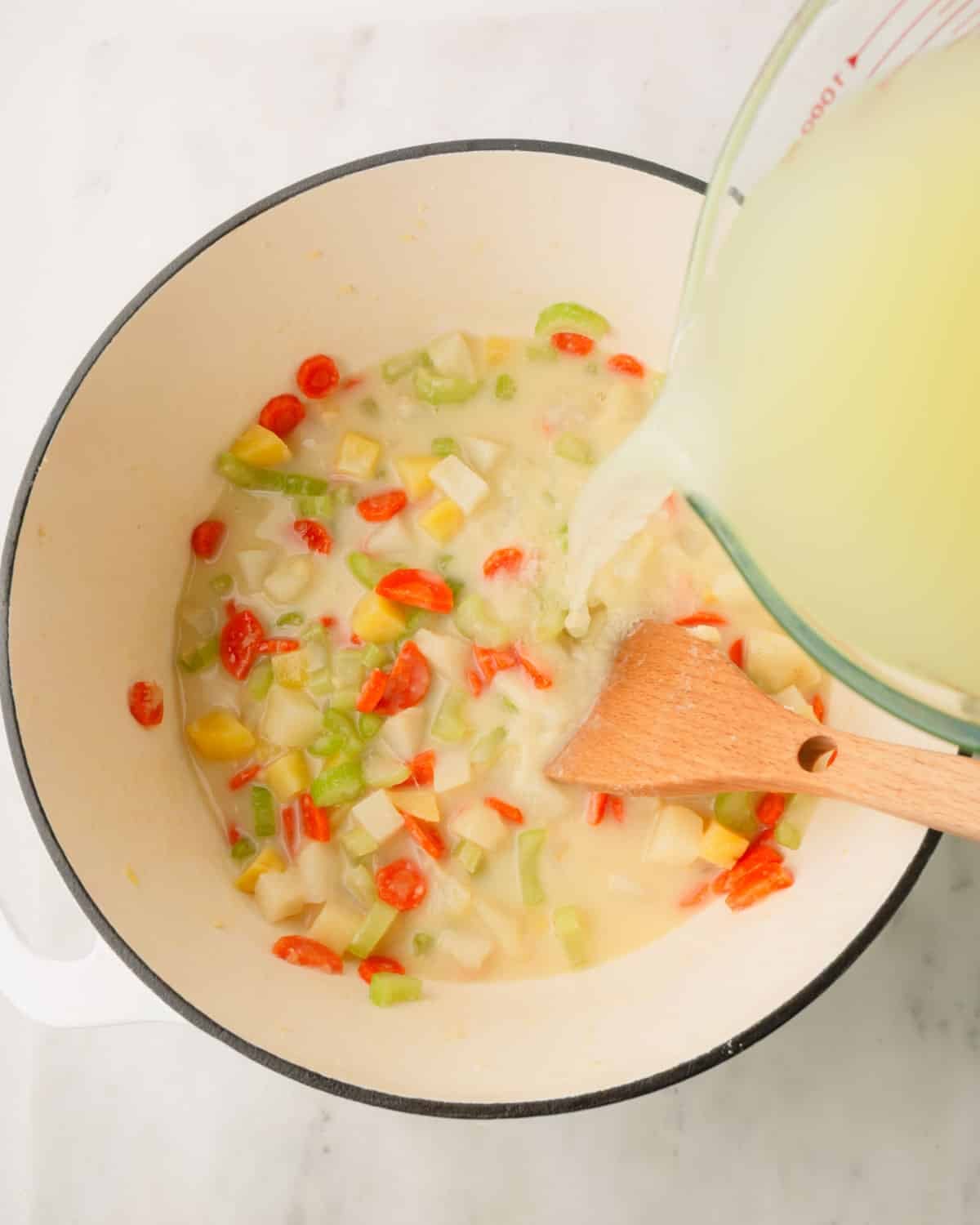 Chicken stock is being poured into a Dutch oven with vegetables.