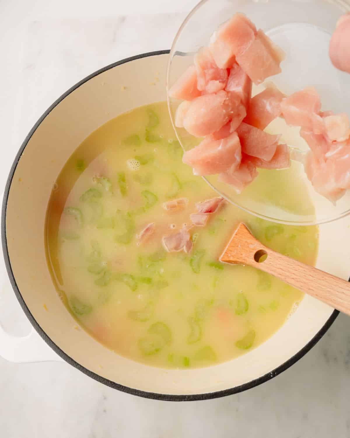 Chicken breast cut into small pieces are being added to the soup in a Dutch oven.