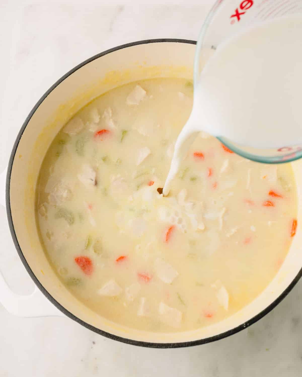 Milk is being poured into the soup in a Dutch oven.