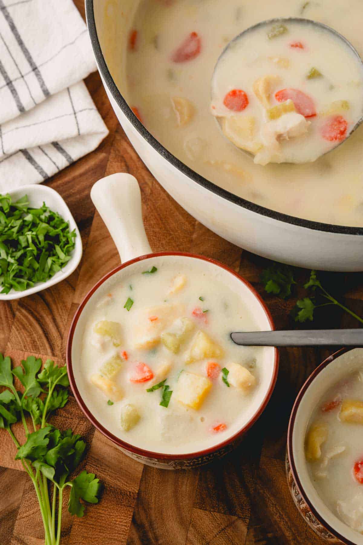 A bowl of knoephla soup next to a pot of soup.