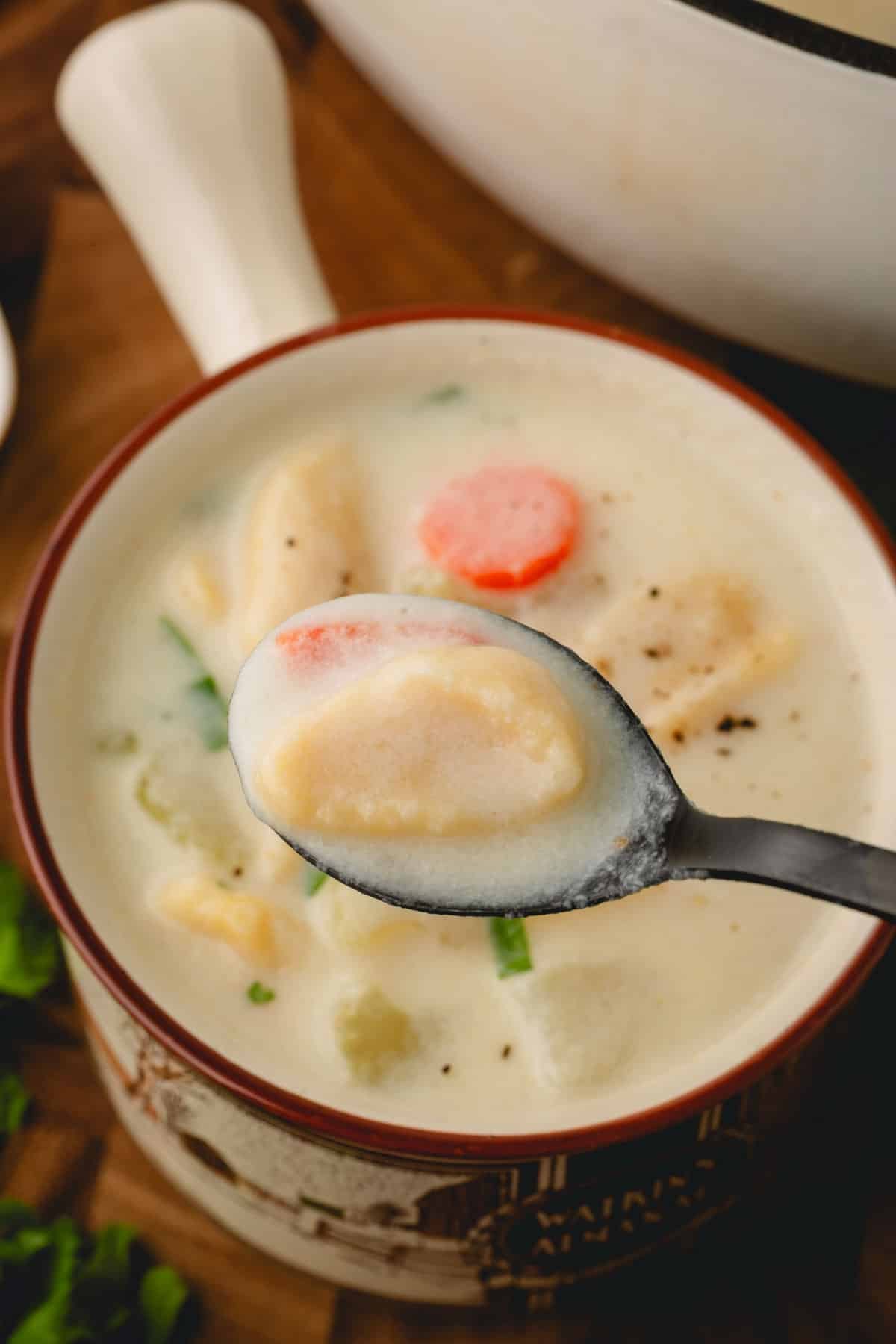 Knoephla with soup and carrot on a spoon lifted over a cup of knoephla soup.