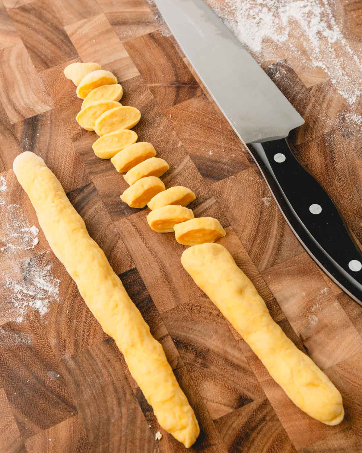 Knoephla dough is rolled into two long, skinny logs, and one log is cut into small pieces.