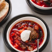 Beef borscht soup in a white bowl topped with dollop of sour cream.