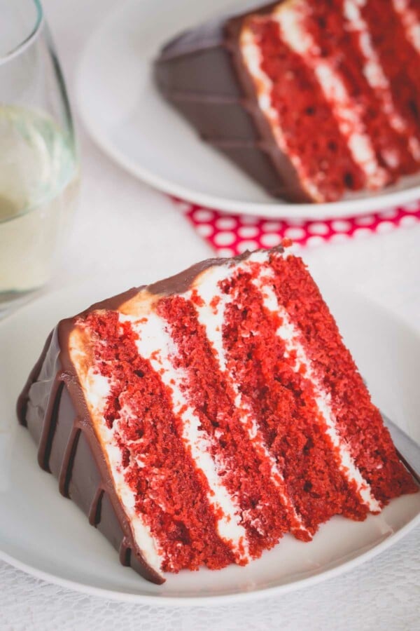 A slice of 4-layer red velvet cake on a white plate.