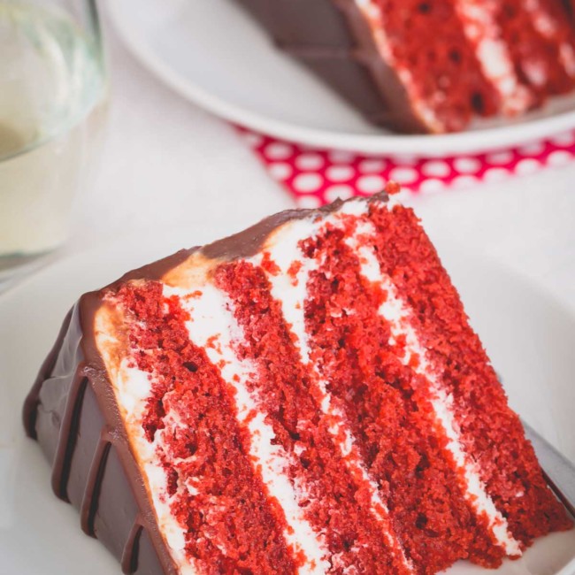A slice of 4-layer red velvet cake on a white plate.