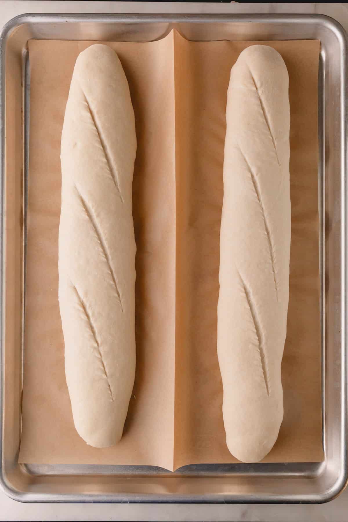 Proofed and scored French bread baguettes on a baking sheet.