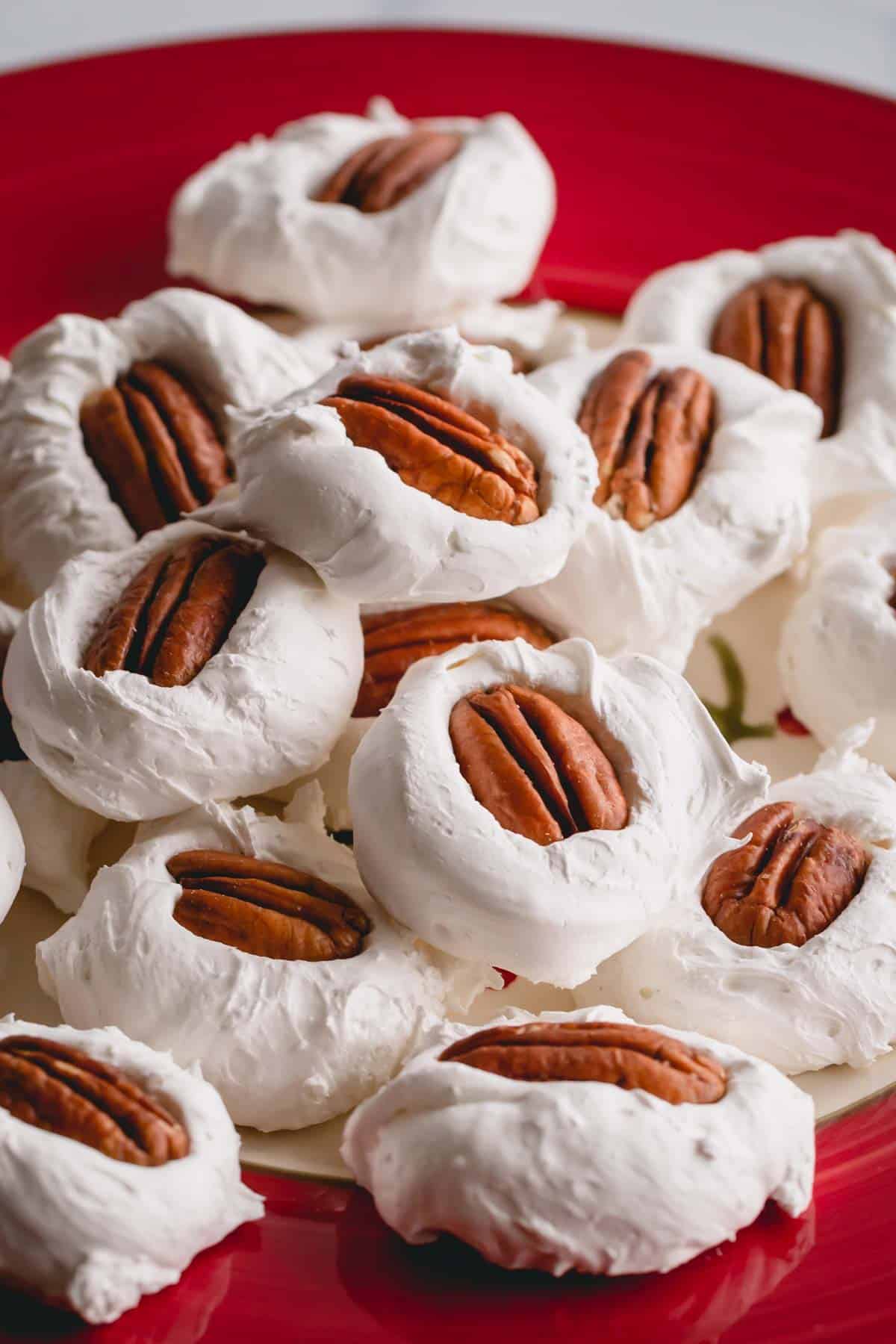 A pile of divinity with pecan halves on top on a red plate.