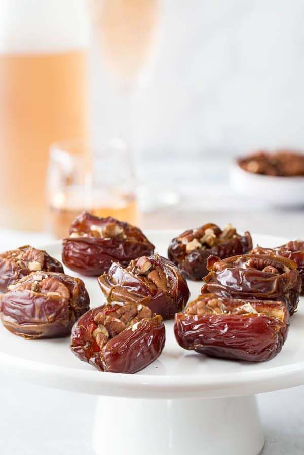 Beautifully arranged roasted dates on a platter with a bottle of wine in the background. Perfect easy appetizer in minutes! #datesnacks #dateappetizer #easyappetizer
