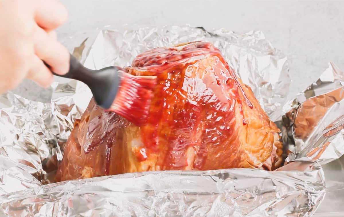 A spiral ham being brushed with raspberry mustard glaze for the first time.