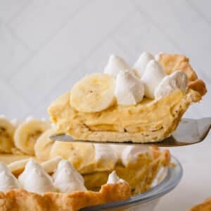 A slice of banana cream pie lifted up from the whole pie.