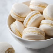 A white bowl of white assembled macarons with white chocolate ganache.