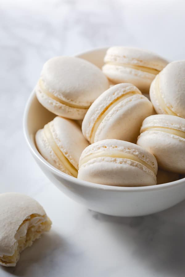 White macarons filled with white chocolate ganache in a white bowl.