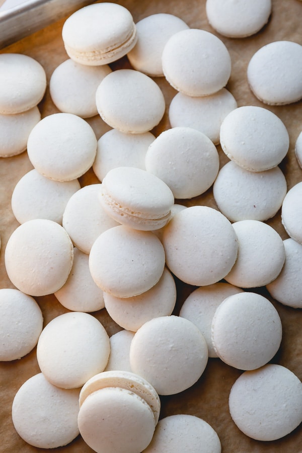 Baked white macaron shells spread out on a baking sheet.