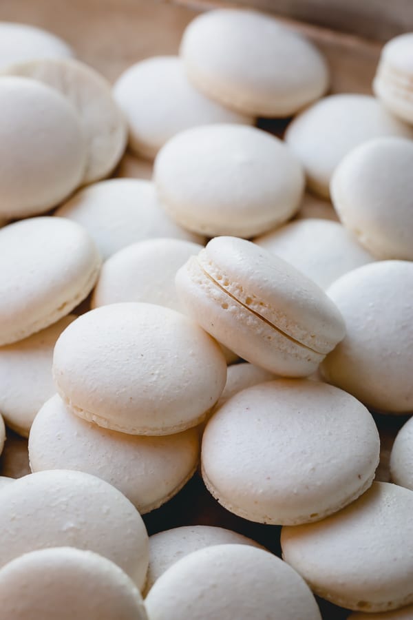 White macaron shells spread out on a baking sheet.