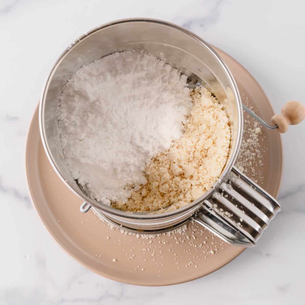 Powdered sugar and almond flour in a hand-crank sift.