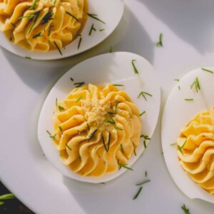 Classic deviled eggs garnished with dill on a white platter.
