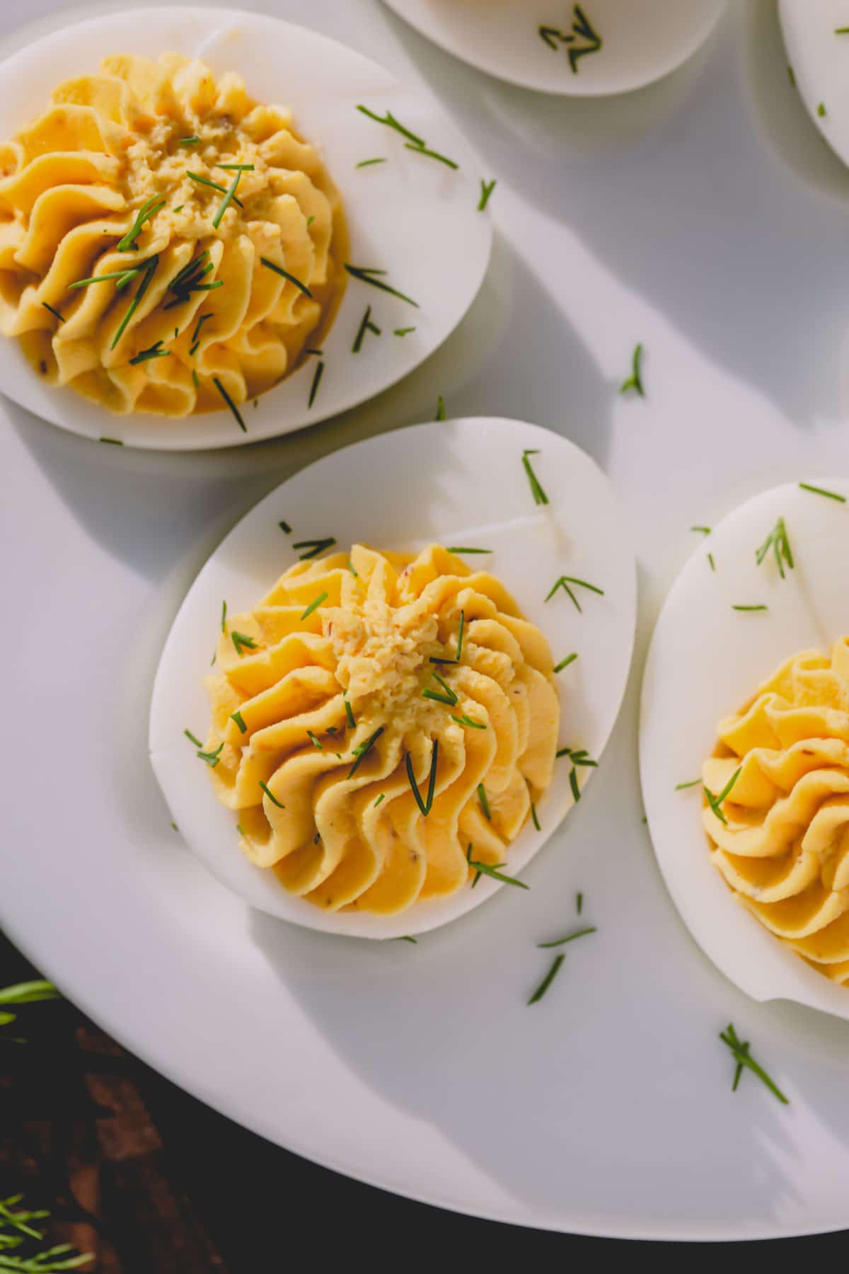 Classic deviled eggs garnished with dill on a white platter.