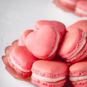 Pink heart-shaped macarons stacked on a plate.