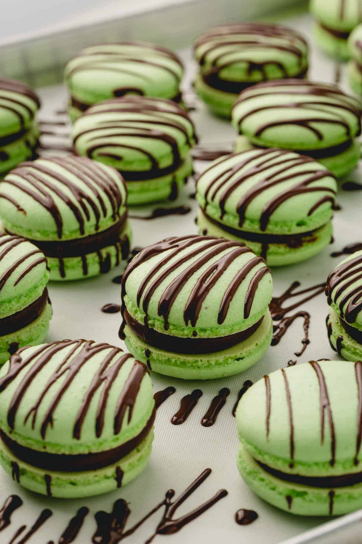 Filled and assembled green macarons drizzled with melted dark chocolate.