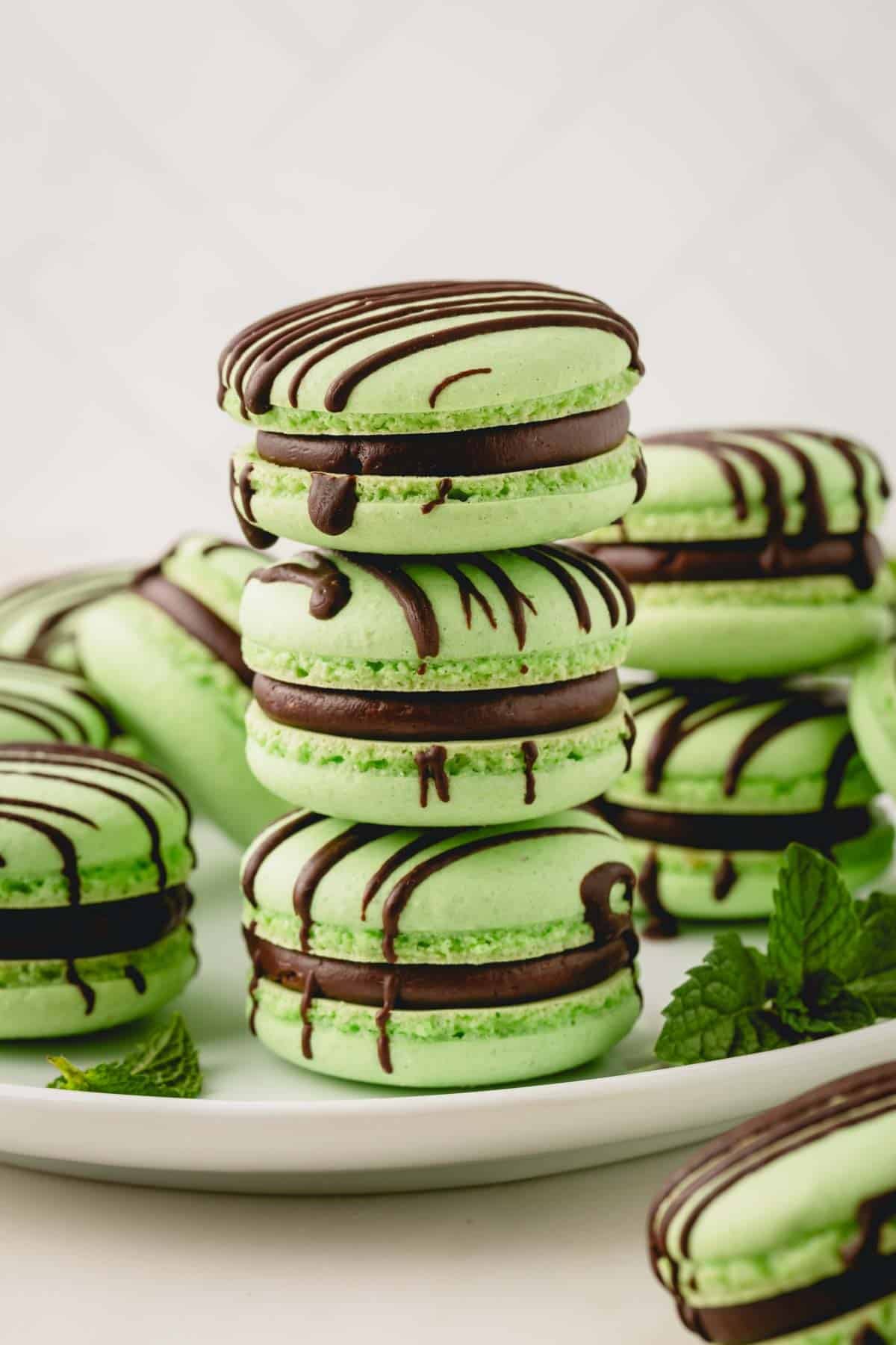 3 mint chocolate macarons stacked on top of each other and surrounded with more green macarons.