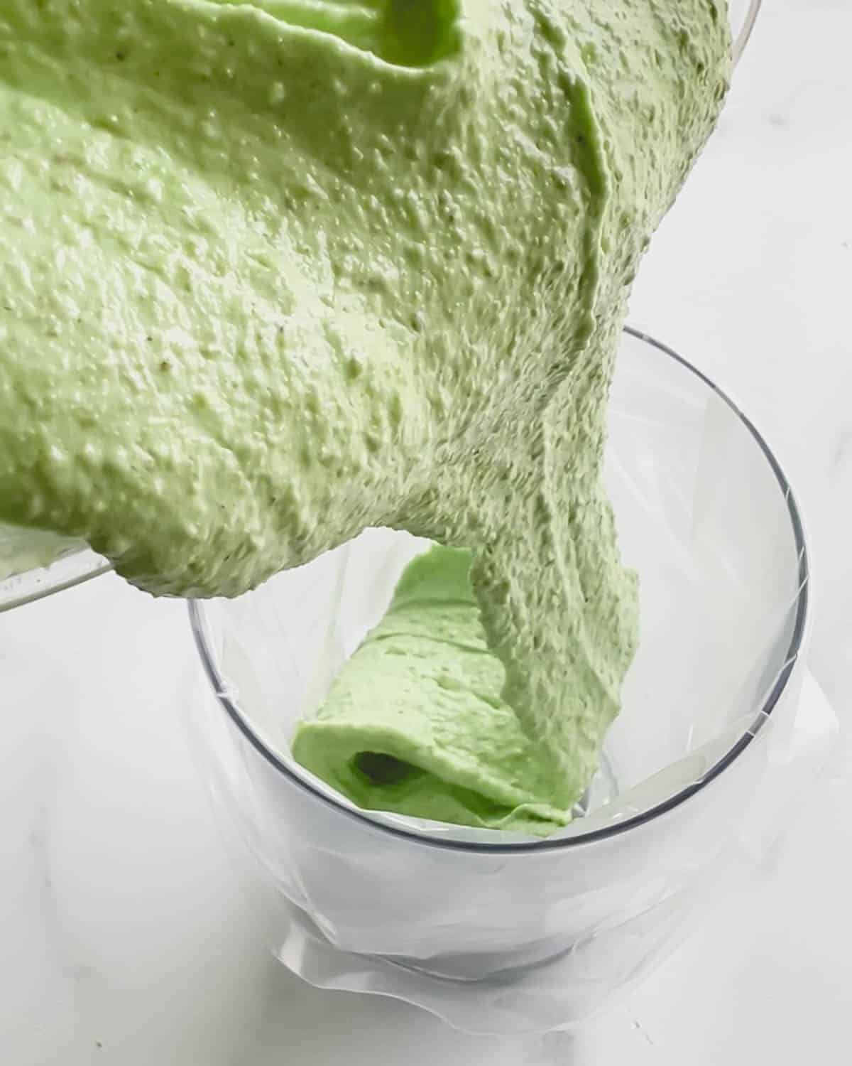 Green macaron batter being poured into a glass fitted with a piping bag.