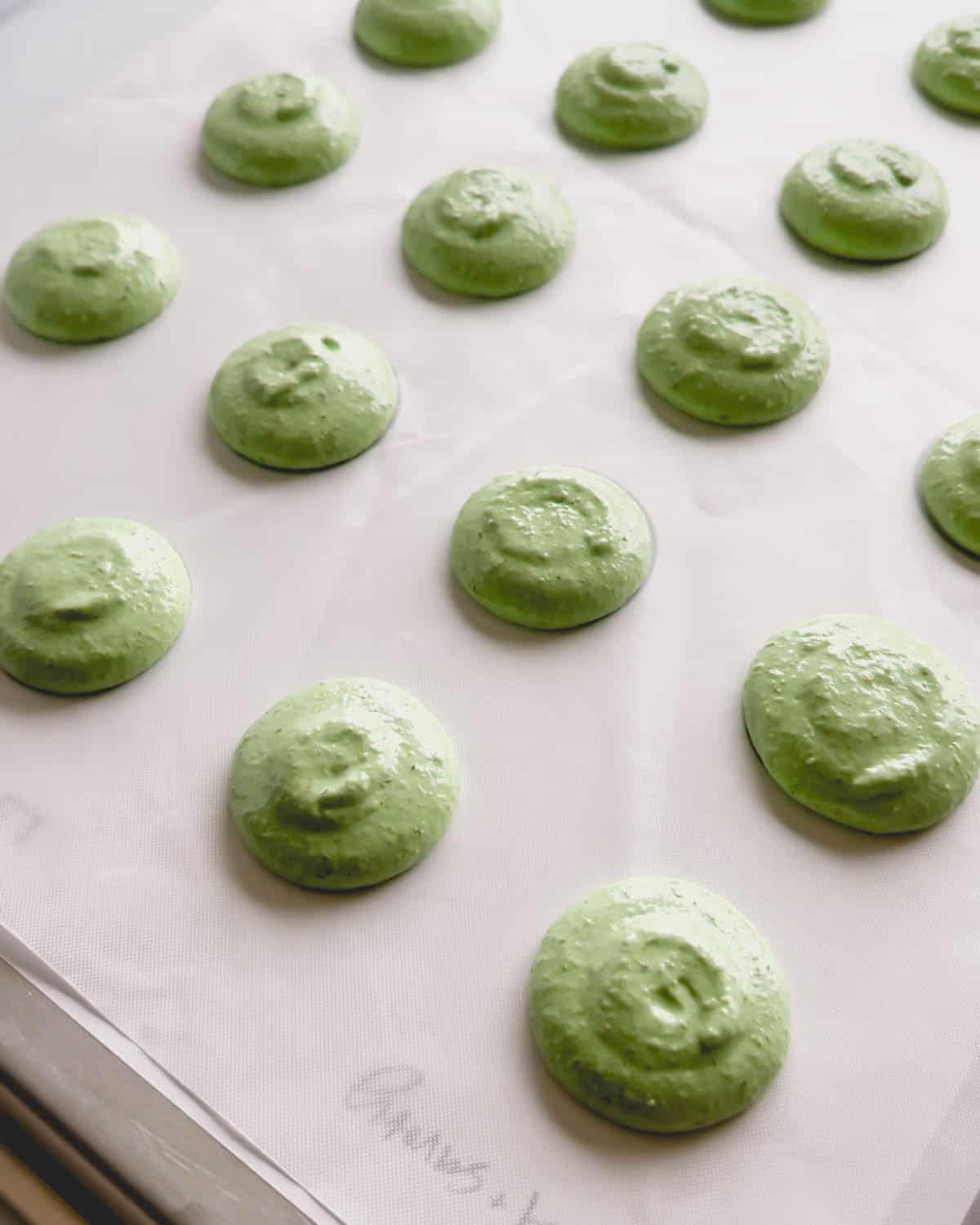 Unbaked green macaron shells on a white surface.