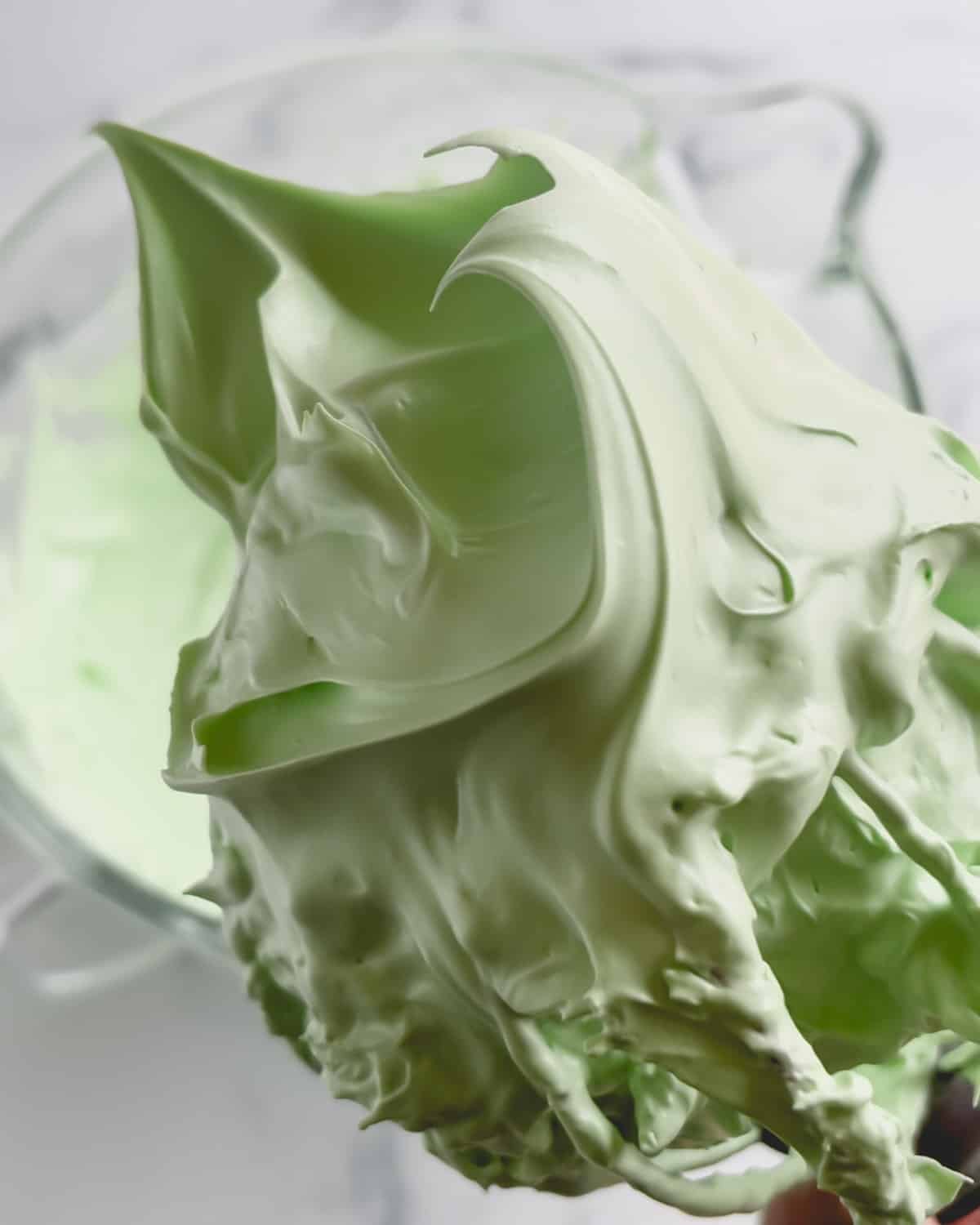 Green meringue with stiff peaks balled up in a whisk.