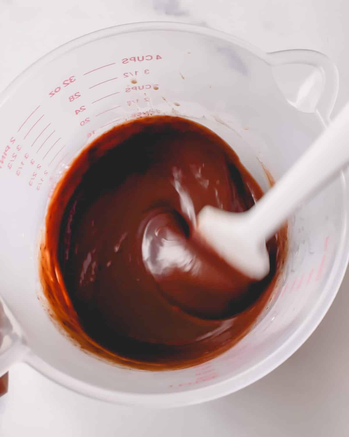 Chocolate ganache in a deep cup being mixed with a spatula.