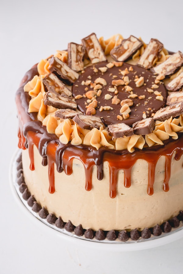 This irresistible Snickers Cake is made of layers of softest chocolate cake, caramel buttercream, peanut butter buttercream, salted caramel and generous amount of crushed peanuts!!! Step by step photos are included for your success! #snickerscake #layercake
