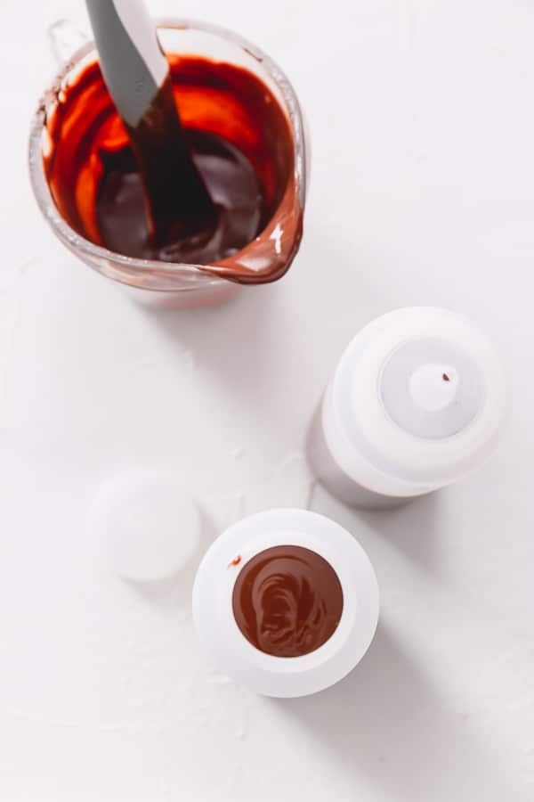 Chocolate ganache in a liquid measuring cup along with 2 plastic squirt bottles.