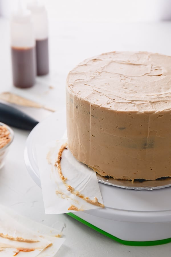 Crumb-coated cake with a parchment paper being pulled out from underneath the cake.