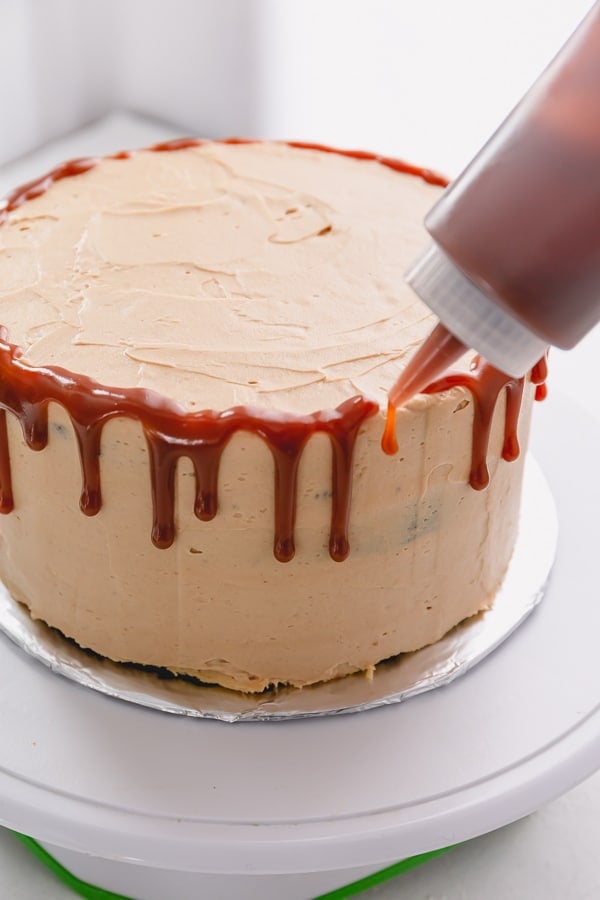 Caramel sauce is being drip along the edges of the cake from a plastic squirt bottle.