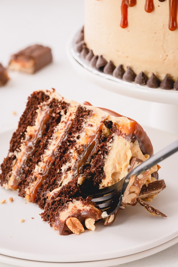 This irresistible Snickers Cake is made of layers of softest chocolate cake, caramel buttercream, peanut butter buttercream, salted caramel and generous amount of crushed peanuts!!! Step by step photos are included for your success! #snickerscake #layercake