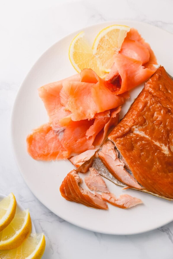 Hot smoked and cold-smoked salmons with couple of slices of lemon on a white plate. There're 2 types of smoked salmon: cold-smoked and hot smoked.