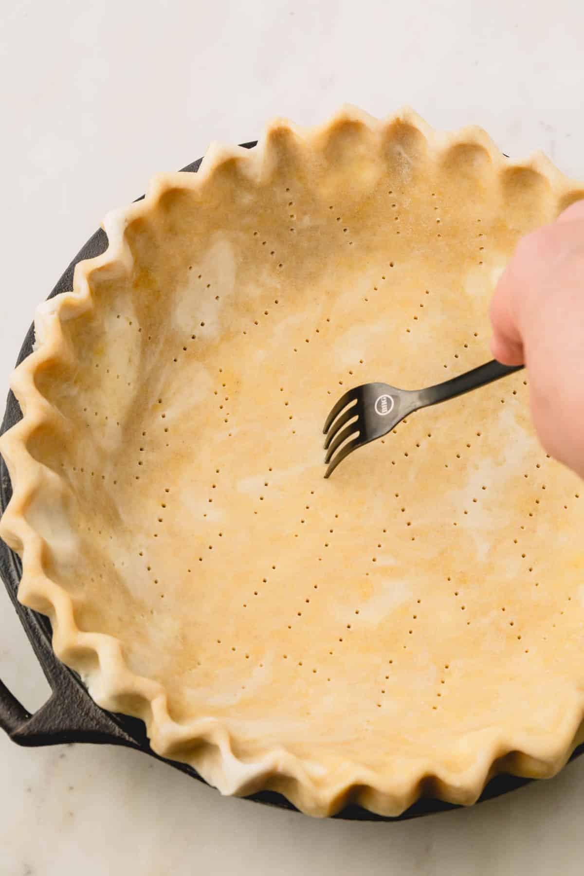 Raw pie crust in a pie dish with crimped edges and with a fork piercing all over the crust.