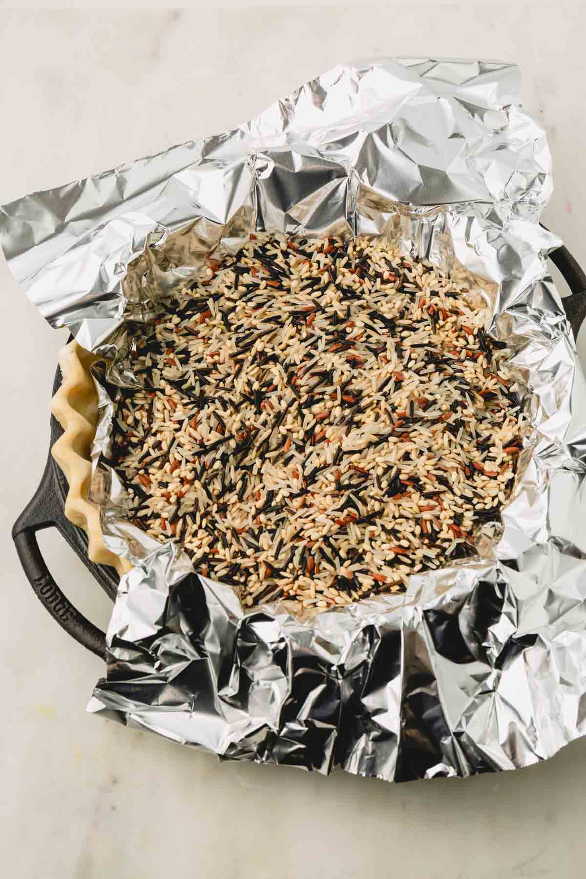 Pir crust in a pie dish covered with foil and filled with raw wild rice mixture.