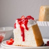 A slice of angel food cake topped with whipped cream and strawberry sauce.