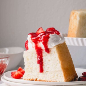 A slice of angel food cake topped with whipped cream and strawberry sauce.